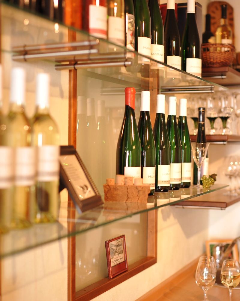 Weinflaschen stehen auf einem Glasregal in einem gemütlichen Weinraum mit Gläsern und Deko an der Wand